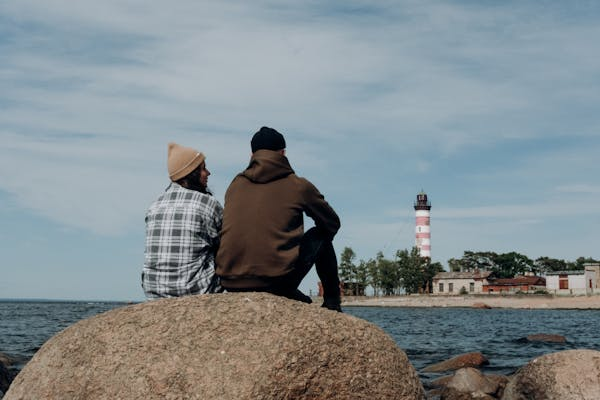 two people sitting on a rock, overlooking distant lighthouse